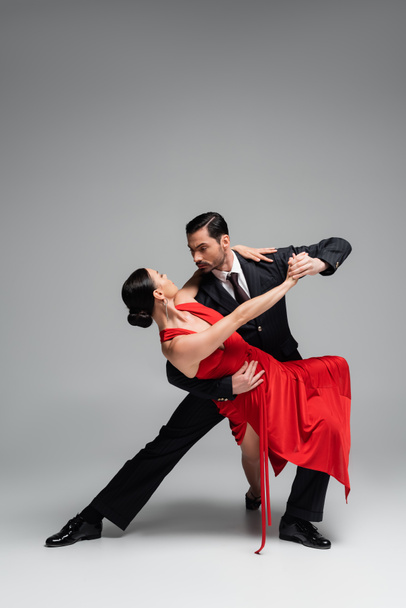 Elegant man in suit dancing tango with partner on grey background - Фото, зображення