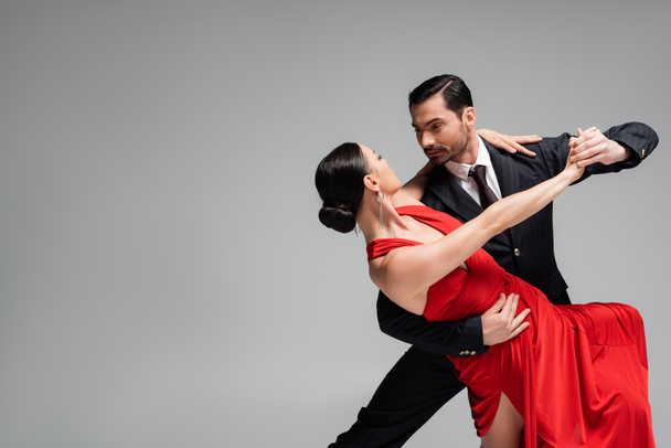 Homme élégant en costume dansant tango avec partenaire isolé sur gris  - Photo, image