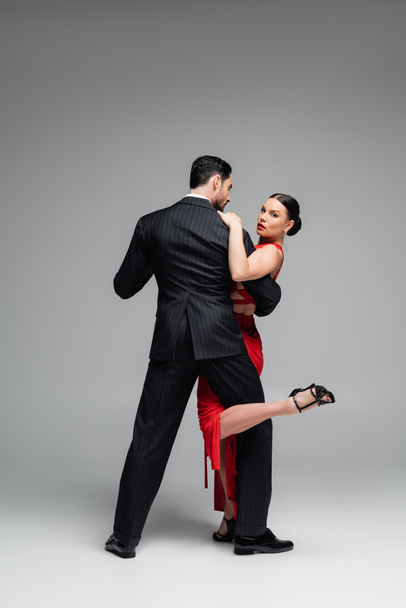 Full length of stylish dancer in heels performing tango with woman on grey background - 写真・画像