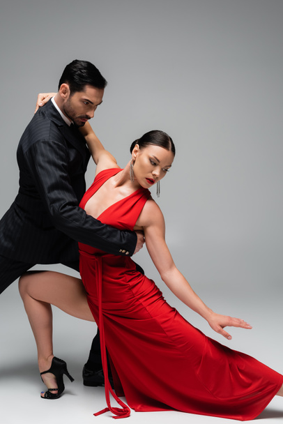 man in elegant pak dansen tango met partner in jurk op grijze achtergrond - Foto, afbeelding