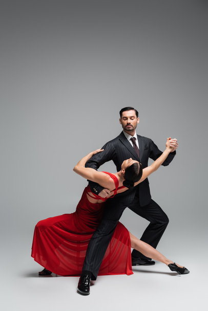 Dancer in suit performing tango with elegant partner on grey background - Photo, Image