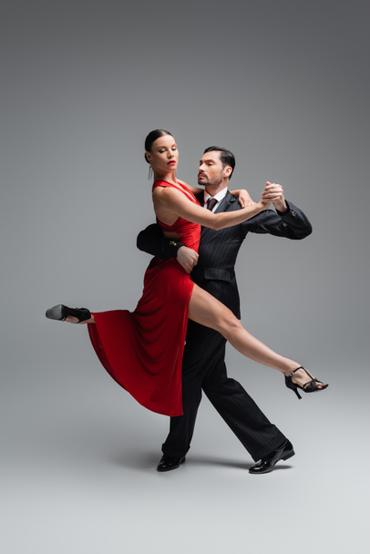 Femme élégante en robe rouge dansant tango avec l'homme sur fond gris - Photo, image