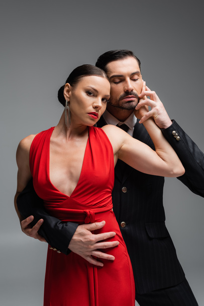 Woman in red dress touching partner while performing tango isolated on grey  - Valokuva, kuva