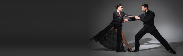 Боковой вид танцоров, держащихся за руки во время танцев на сером фоне с тенью, баннером  - Фото, изображение