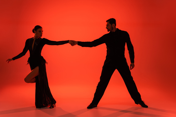 Silueta de bailarines de salón tomados de la mano sobre fondo rojo con sombra  - Foto, Imagen