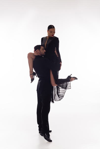 Brunette dancer lifting partner in black dress on white background  - Foto, imagen
