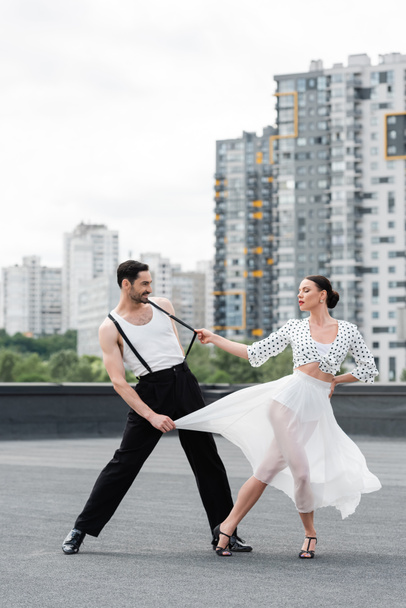 Stylische Frau in High Heels tanzt mit lächelndem Partner auf Hausdach  - Foto, Bild