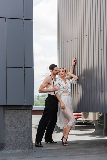ダンサーは昼間の建物の屋上にヒールとスカートの笑みを浮かべてパートナーを抱きしめる  - 写真・画像