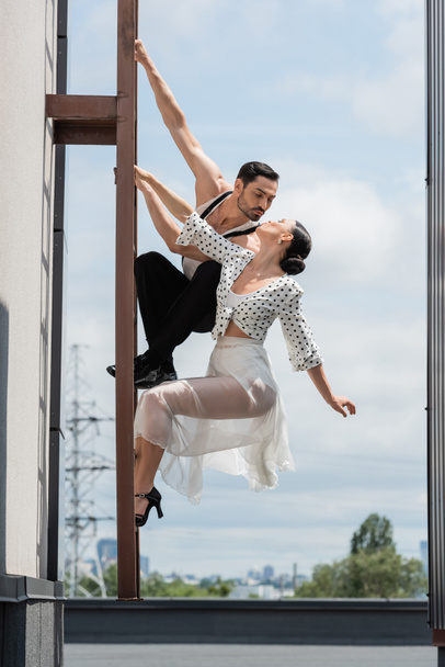Professional dancers kissing while posing on ladder on rooftop of building at daytime  - Fotografie, Obrázek