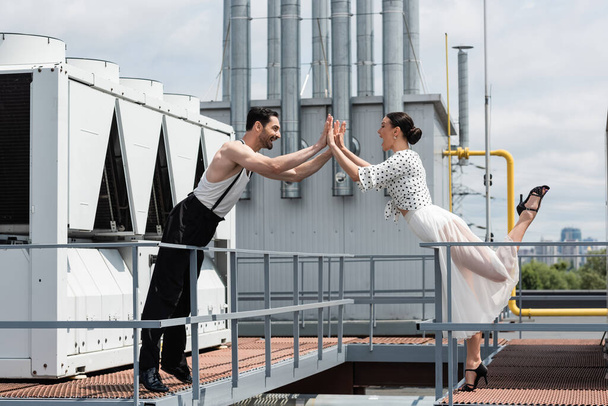 Zijaanzicht van opgewonden professionele dansers geven high five op het dak van het gebouw  - Foto, afbeelding