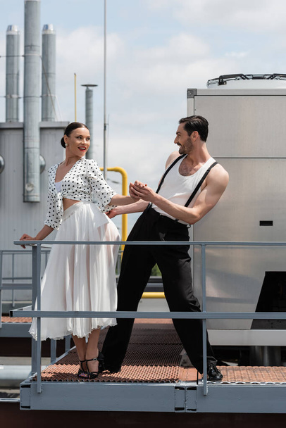 Cheerful dancers holding hands while moving near railing on roof of building outdoors  - Foto, Imagen