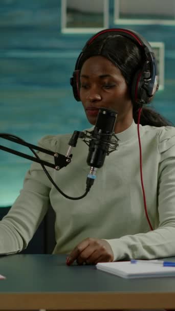 Dikey video: Siyahi blogcu kadın blogu için stüdyosunda video kaydediyor ve mikserdeki sesleri kontrol ediyor. Online prodüksiyon internet yayınları sunucunun canlı yayın içeriğini gösteriyor - Video, Çekim