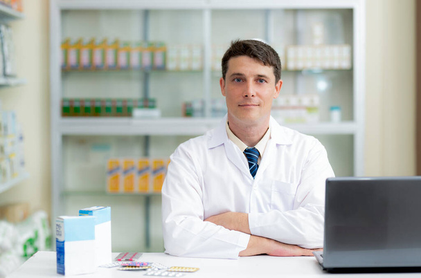 Young man caucasian pharmacist in pharmacy, drug consultant, front view looking at camera. - Photo, image