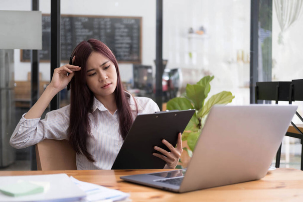 Азиатская бизнесвумен серьезно настроена на работу, вызывая головную боль из-за документов с ноутбуком в офисе... - Фото, изображение