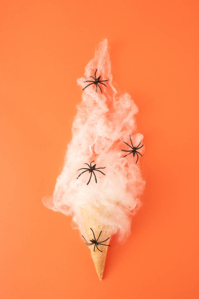オレンジ色の背景に黒いクモとアイスクリームコーンと白いクモの巣。最小限のハロウィントリックと治療の概念. - 写真・画像
