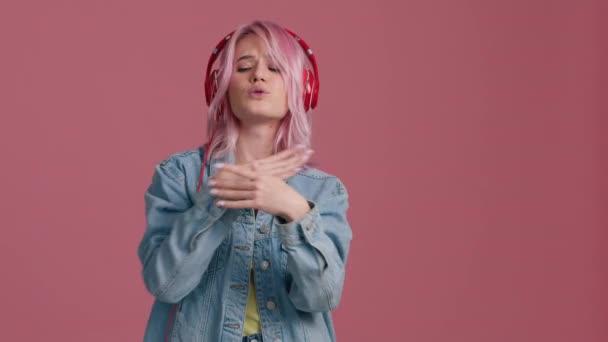 Portret van hippe tiener mooie mode meisje model zingen lied in stijlvolle hoofdtelefoon genieten van dansen, luisteren coole muziek in roze studio achtergrond in trendy stijlvolle denim jas geel top slow mo - Video