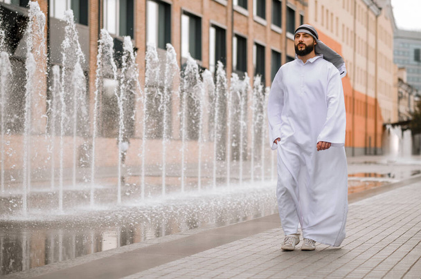 In office district. Middle eastern young man in traditional clothing walking along the street - Foto, Imagen