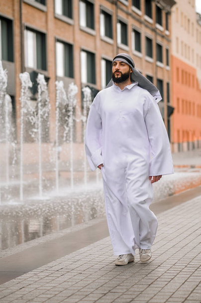 En el distrito de oficinas. Hombre joven de Oriente Medio con ropa tradicional caminando por la calle - Foto, Imagen