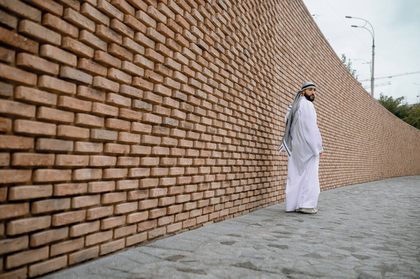 Man op straat. Man in wit lang thobe op een baksteen muur achtergrond - Foto, afbeelding