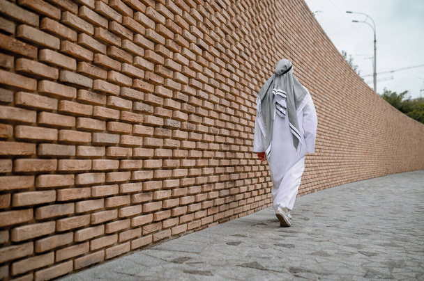 Человек на улице. Человек в белом длинном тобе на фоне кирпичной стены - Фото, изображение