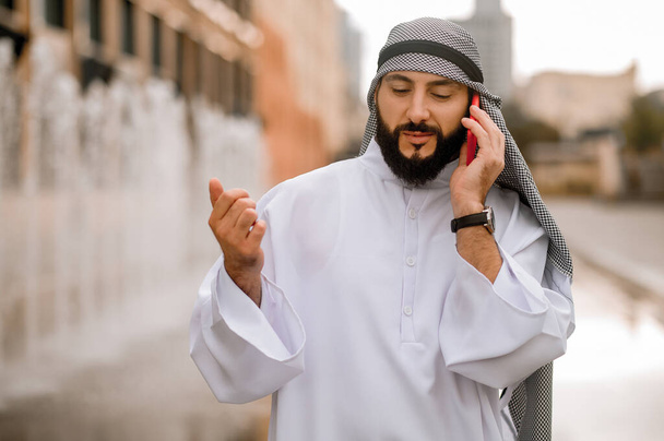 Moderner Mittlerer Osten. Mann in kaffiyeh und thobe mit einem Telefon in der Hand - Foto, Bild