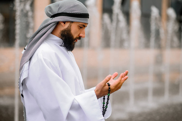 Oración. Joven hombre árabe barbudo con ropa tradicional rezando - Foto, Imagen