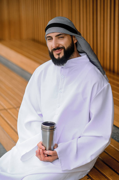 Feeling quiet. Young arabian man sitting on a wooden bench with metal - Photo, Image