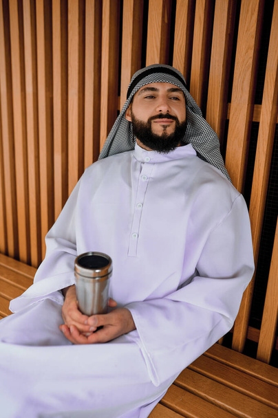 Pauza na kafe. Mladý arabský muž sedí na dřevěné lavičce - Fotografie, Obrázek