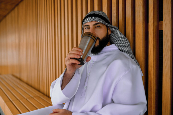 Kahve molası. Tahta bir bankta oturan genç bir Arap. - Fotoğraf, Görsel