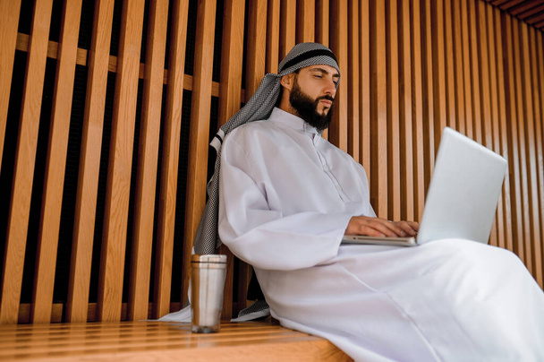 仕事中だ。若いアラビア人のビジネスマンがノートパソコンで仕事をしていて - 写真・画像
