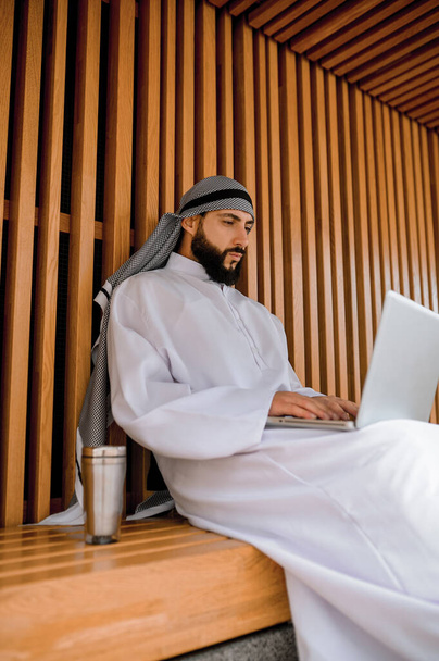 Çalışıyorum. Genç Arap iş adamı bir dizüstü bilgisayarda çalışıyor ve olaya dahil olmak istiyor. - Fotoğraf, Görsel
