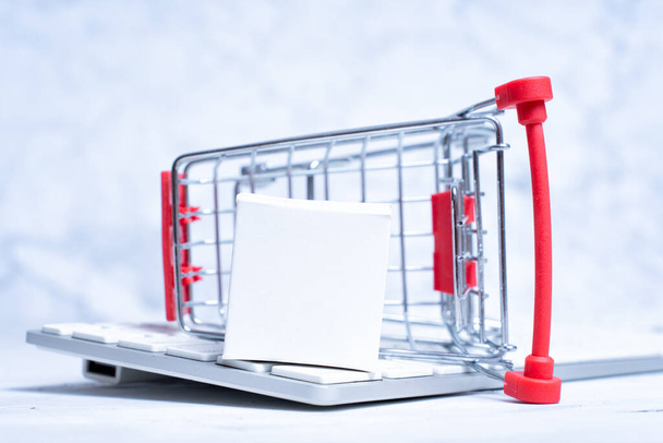 Overturned miniature shopping trolley and tiny delivery box placed on a keyboard. Creative online shopping concept. - Фото, зображення