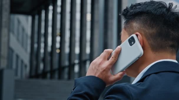 Powrót widok z tyłu nierozpoznawalny Azjata w formalnym garniturze stoi w mieście rozmawiając rozmowy telefoniczne ze smartfonem szef lider przedsiębiorca przedsiębiorca pracodawca na świeżym powietrzu rozmowy mobilne - Materiał filmowy, wideo