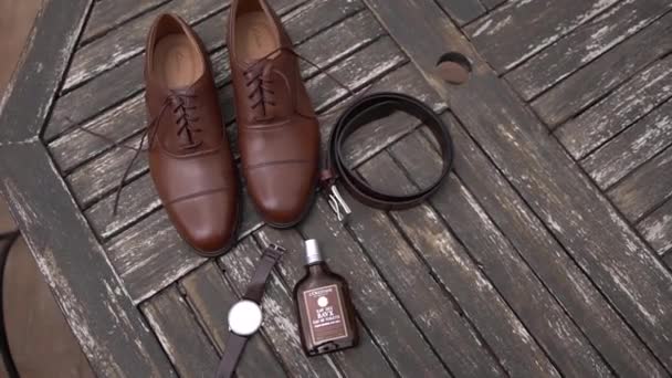 Hombres zapatos, cinturón, reloj y perfume se encuentran en una mesa de madera. Imágenes FullHD de alta calidad - Metraje, vídeo