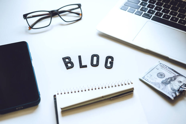 Hogyan kezdjünk Blog, Blogolás kezdőknek. Pénzzé teszi a blogodat. Blog szó az asztalon laptop, okostelefon, nyitott notebook, dollár bankjegyek és szemüveg. - Fotó, kép