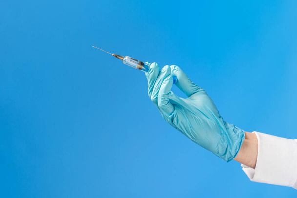 Hand in a blue rubber glove holding a syringe ona blue background. Medical injection concept. - Foto, Imagen