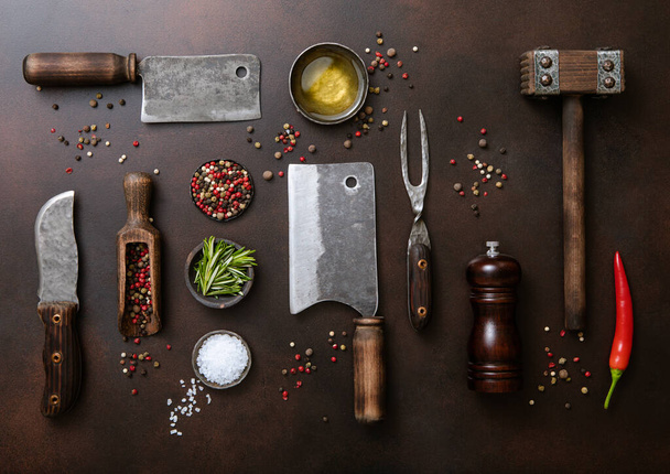 Meat cleavers,tenderizer,fork,knife and other kitchen meat utensils with oil,herbs,salt and pepper on dark kitchen table background. - 写真・画像
