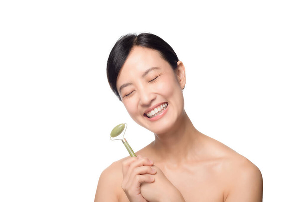 Studio shot of an attractive young asian woman using a jade roller on her face against a white background - Foto, immagini