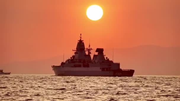Silhouette Of Warship In The Sunset es un impresionante video de archivo que cuenta con imágenes de buques de guerra y transbordadores pasando por el cielo rojo y el sol se pone.  - Metraje, vídeo