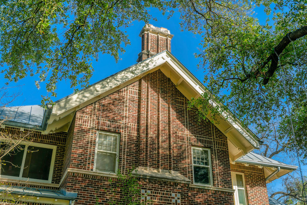 Buitenaanzicht van een huis met rode bakstenen muur en geveldak in San Antonio Texas. Schuifglazen ramen en schoorsteen zijn ook te zien op de gevel met helderblauwe lucht achtergrond. - Foto, afbeelding