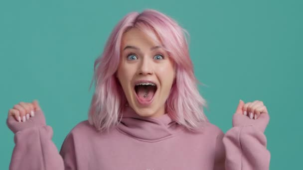 Удивлённая, взволнованная молодая женщина с модной розовой прической, удивленно поднимающая руки, глядя в камеру и стряхивая с себя волосы с положительной улыбкой, шокированная неожиданными новостями. Студия изолированный фон 4K - Кадры, видео