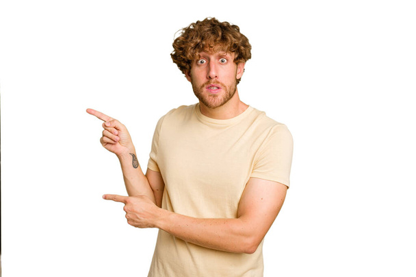 Young caucasian man isolated on green chroma background shocked pointing with index fingers to a copy space. - Photo, Image