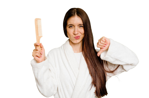 Young caucasian woman holding an hair comb isolated showing a dislike gesture, thumbs down. Disagreement concept. - Photo, Image