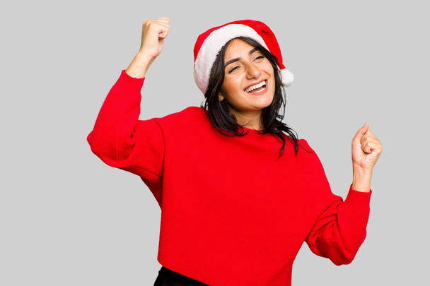 Giovane donna indiana che celebra il Natale indossando un cappello da Babbo Natale isolato alzando il pugno dopo una vittoria, concetto vincitore. - Foto, immagini