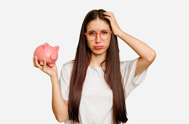 Young caucasian woman holding a piggy bank isolated being shocked, she has remembered important meeting. - Foto, imagen