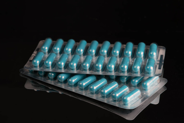 Blauwe medische capsules in blaren geïsoleerd op een zwarte achtergrond. Selectieve focus.   - Foto, afbeelding