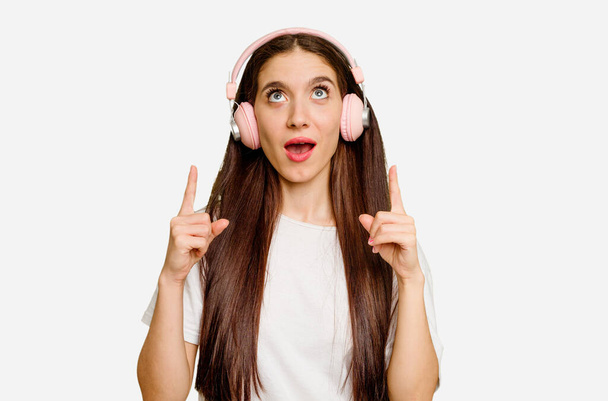 Junge kaukasische Frau trägt Kopfhörer isoliert und zeigt kopfüber mit geöffnetem Mund. - Foto, Bild