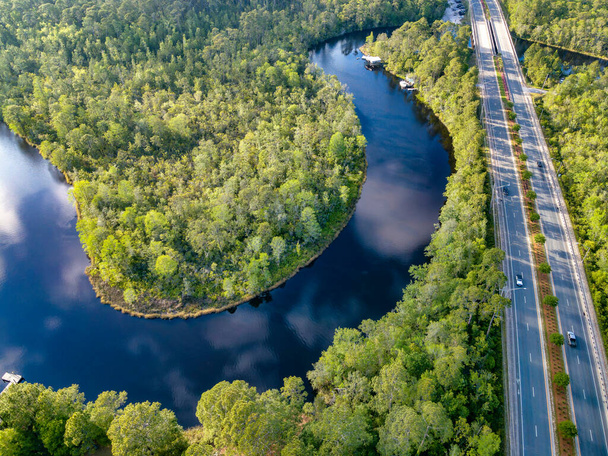Река Ист-Бэй протекает по пышным лесам и дорогам Наварры во Флориде. Вид с воздуха на воду, буйную зеленую листву и дорогу с машинами в солнечный день. - Фото, изображение