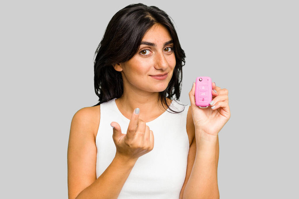 Jeune femme indienne tenant une voiture clés isolées pointant avec le doigt vers vous comme si inviter se rapprocher. - Photo, image