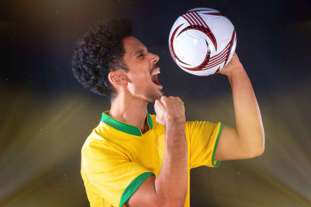 Giocatore di calcio brasiliano nero che tiene la palla e celebra, isolato su sfondo nero. - Foto, immagini
